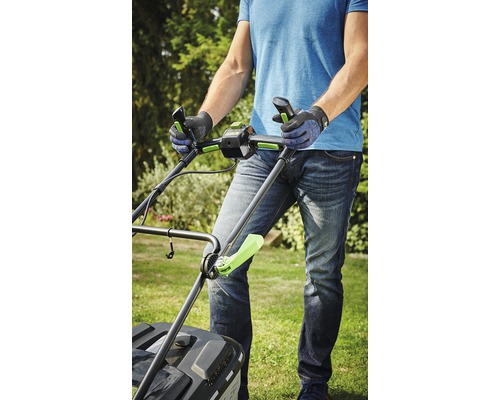 O persoană manevrează o mașină de tuns iarba în grădină.