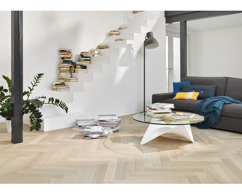 Cameră de zi cu parchet deschis la culoare în model herringbone, scară cu cărți și canapea gri