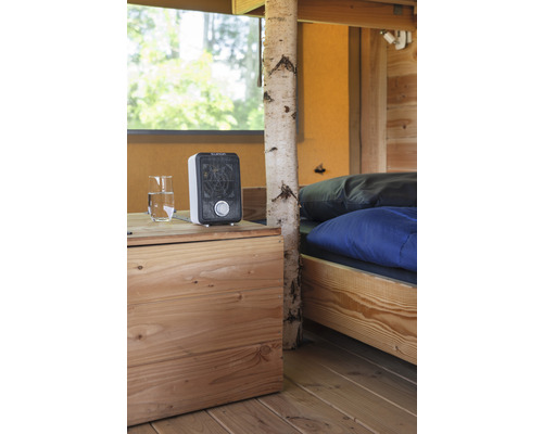 Interior cu pat, podea din lemn, noptieră, pahar cu apă și aerotermă