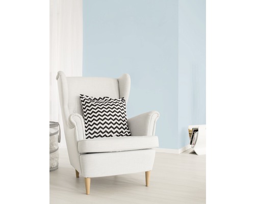 Cameră de zi luminoasă cu vopsea de perete albastru pastel, fotoliu alb și pernă cu model în zigzag