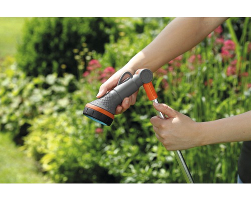 Furtun de grădină cu cap de pulverizare în mână în fața plantelor verzi