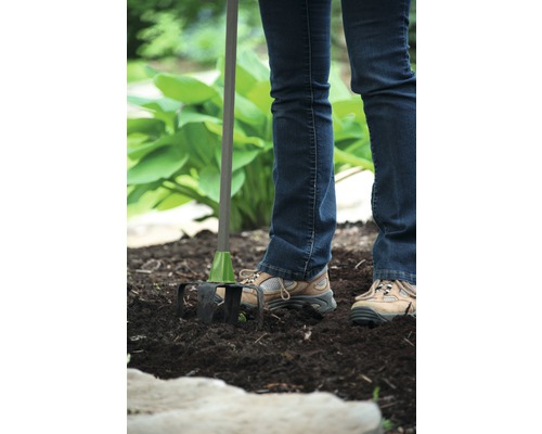 O persoană folosește un cultivator în grădină pentru a afâna solul.