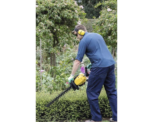 Un bărbat taie un gard viu cu un tăietor de gard viu în grădină.