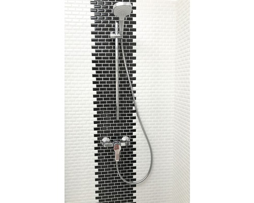 Baterie de duș cu duș de mână în fața peretelui cu gresie neagră și albă