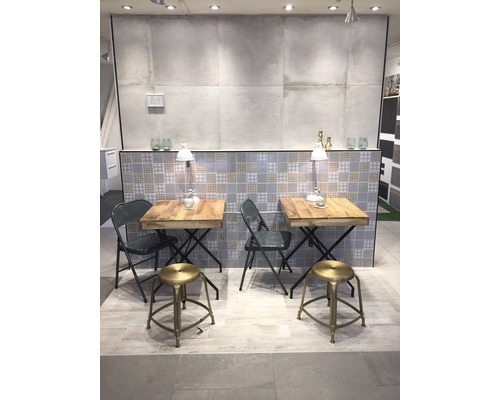 Sală de expoziție cu două mese și scaune, fundal cu gresie și iluminare.