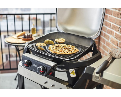 Grătar Weber cu mâncare pe grătar și pe o masă în fundal