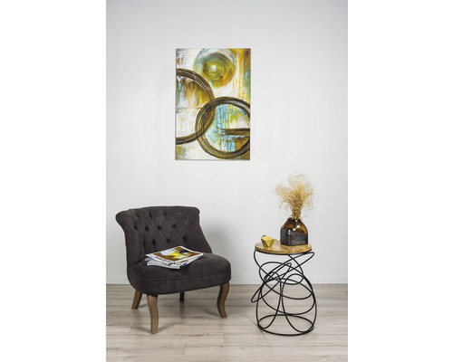 Scenă cu un tablou cu motive circulare abstracte, un fotoliu și o măsuță laterală cu decorațiuni.