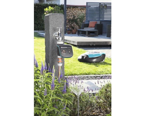 Scenă cu un robinet, un computer de irigare Gardena, un aspersor de gazon și un robot de tuns iarba în grădină.
