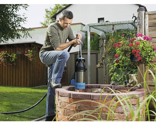 Un bărbat operează o pompă de puț adânc la un puț din grădină.