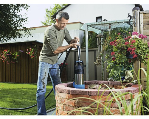 Un bărbat operează o pompă manuală cu piston la fântâna din grădină.