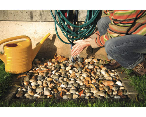 Scenă de udare a grădinii cu stropitoare galbenă, furtun de apă și persoană care se spală pe mâini