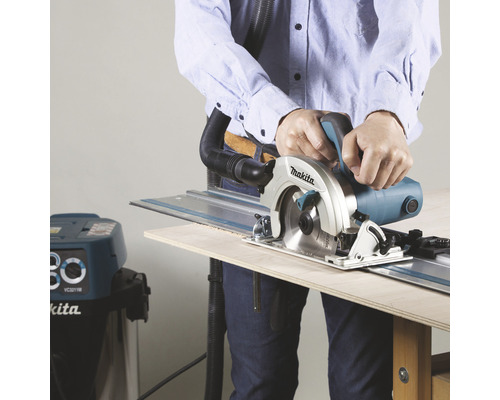 Un bărbat taie lemn cu un fierăstrău circular portabil Makita și șină de ghidare, conectate la un aspirator