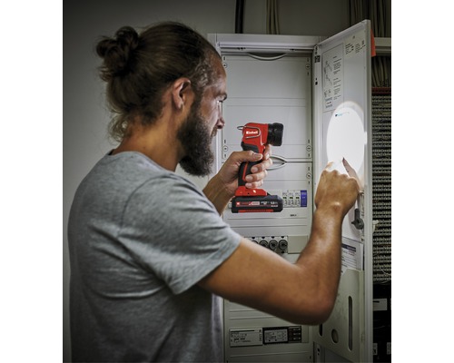 Un bărbat iluminează o cutie de siguranțe cu o lampă cu acumulator.