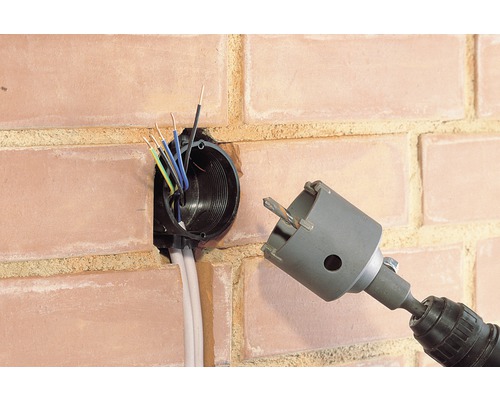 Mașină de găurit cu ferăstrău carotier lângă o priză de perete într-un zid de cărămidă