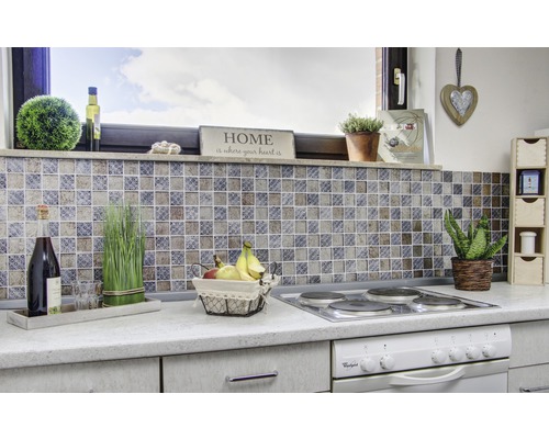 Scenă de bucătărie cu plăci de mozaic, plită, decorațiuni și produse alimentare pe un blat.