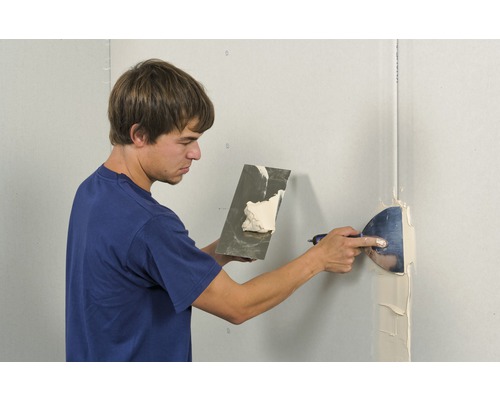 Bărbat care chituește un perete cu chit și o spatulă