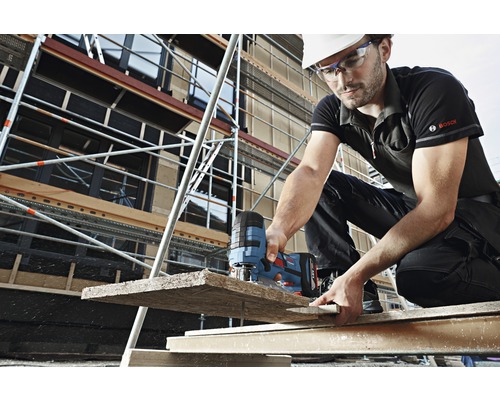 Un bărbat taie o bucată de lemn cu un ferăstrău vertical pe un șantier.