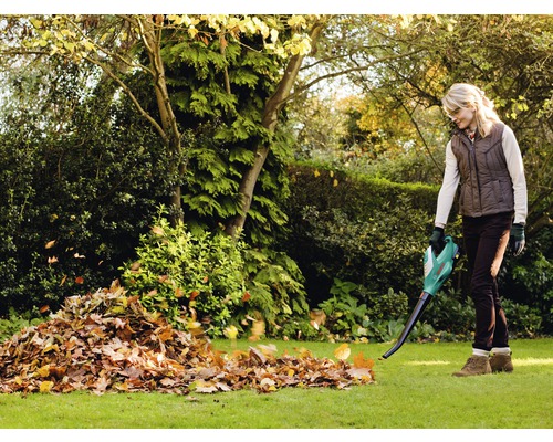 Femeie folosind o suflantă de frunze în grădină pentru a îndepărta frunzele.