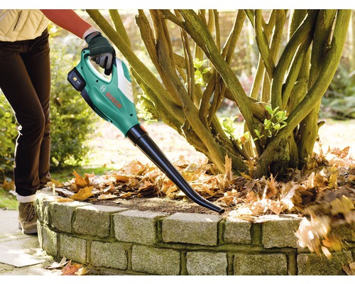 O persoană folosește o suflantă de frunze fără fir Bosch pentru a îndepărta frunzele dintr-un strat de flori.