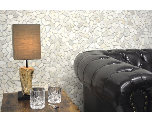 Scenă cu o lampă de masă pe o masă de lemn, două pahare, un deschizător de sticle și o canapea de piele în fața unui perete cu pietre de râu.