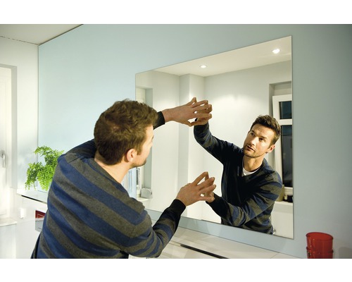 Bărbat fixând o oglindă dreptunghiulară pe perete