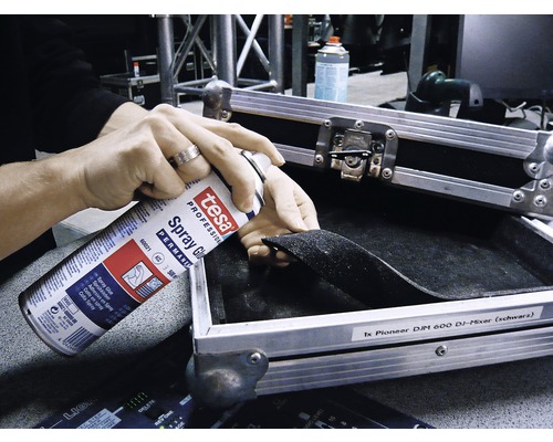 O persoană pulverizează adeziv spray într-o cutie de scule.