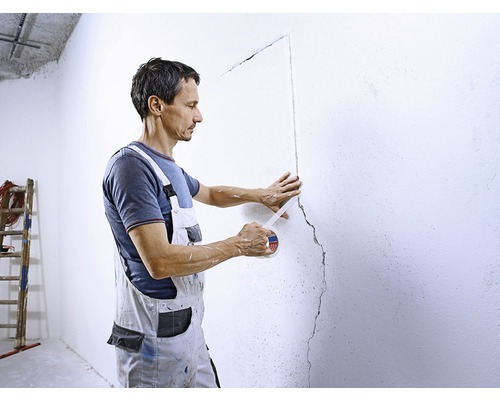 Un bărbat acoperă un perete cu bandă adezivă pentru a ascunde o fisură.