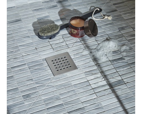 Prim-plan cu un duș cu gresie, scurgere de duș, perie, aditiv de baie și spumă de săpun