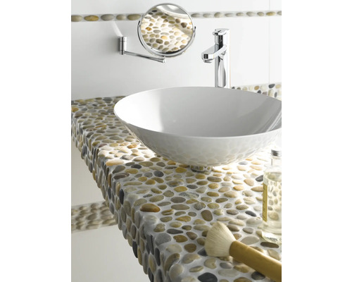 Scenă de baie cu lavoar așezat pe blat, robinet, oglindă de perete și raft cu pietricele