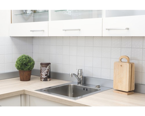 Scenă de bucătărie cu chiuvetă, robinet, tocătoare și decorațiuni pe un blat de lucru deschis la culoare, în fața unui perete cu faianță albă