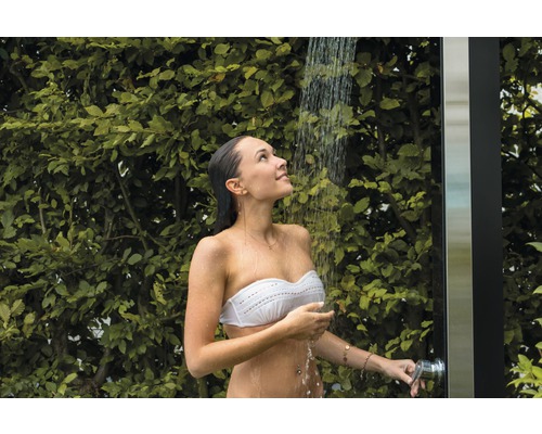Femeie sub duș de grădină cu plante verzi în fundal