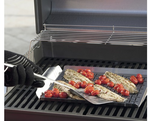 Pește și roșii preparate pe o placă de grătar cu o spatulă pe un grătar.