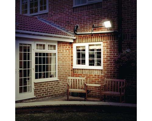 Exteriorul unei case cu fațadă din cărămidă, iluminată de un reflector LED montat pe perete