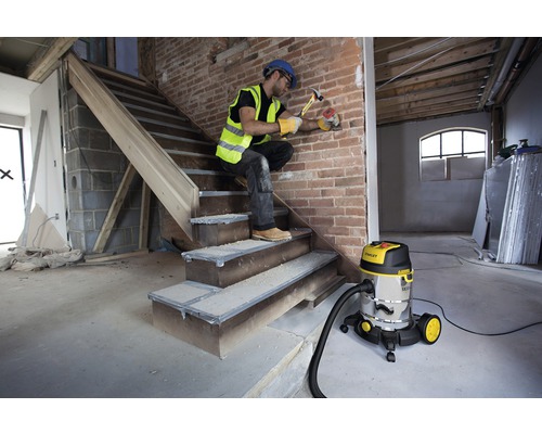 Artizan care efectuează lucrări de construcție cu un aspirator umed-uscat pentru curățarea zonei de lucru