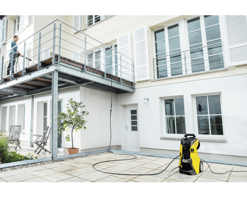 Femeie curăță terasa cu un aparat de curățat cu înaltă presiune în fața fațadei casei