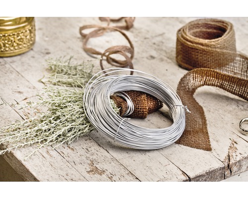 Scenă decorativă cu sârmă de legat, bandă de iută și ramuri verzi pe o masă de lemn