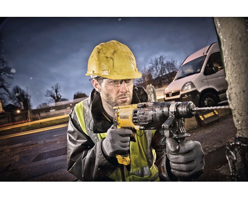 Un muncitor în construcții cu cască de protecție găurește un obiect în aer liber cu o mașină de găurit.