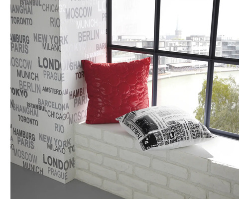 Interior decorativ cu o pernă roșie și una alb-negru pe un pervaz în fața unui perete imprimat cu nume de orașe