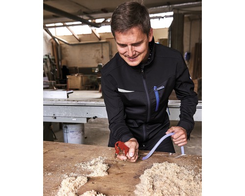 Un bărbat în haine de lucru folosește un pistol de suflat pe o masă cu așchii de lemn.