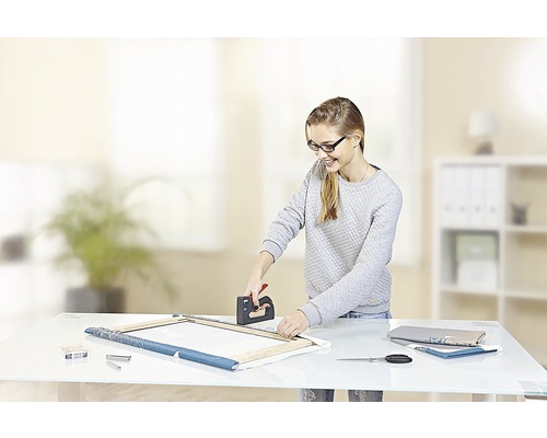 Femeie care folosește un capsator pentru a întinde o pânză pe un cadru.