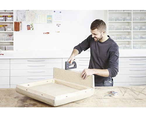 Un bărbat fixează tapițeria cu un capsator manual pe o piesă de mobilier.