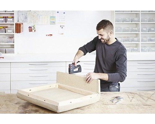 Bărbat fixează tapițeria de o piesă de mobilier cu un capsator manual