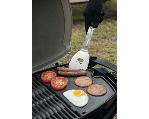 Grătar cu cârnați, roșii, slănină și un ou prăjit, plus o persoană cu o spatulă