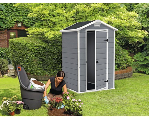 Scenă cu o femeie plantând flori în grădină, un cărucior cu pământ și o magazie de grădină gri cu ușa deschisă