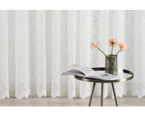 Cortină decorativă albă cu broderie lângă o măsuță laterală cu flori