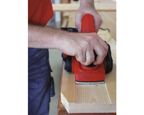 O persoană rindeluiește o scândură de lemn cu o rindea electrică.