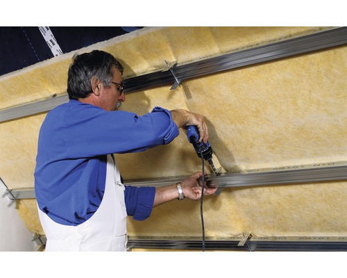 Un bărbat fixează izolație termică cu o șurubelniță fără fir pe o substructură.