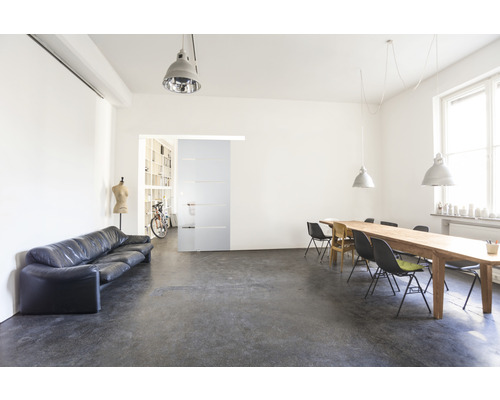 Fotografie de interior a unei camere luminoase cu canapea, masă și ușă glisantă