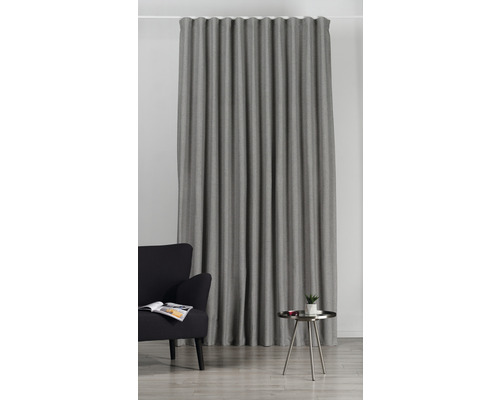 Perdea gri din material textil cu pliuri într-un living cu fotoliu și măsuță laterală.