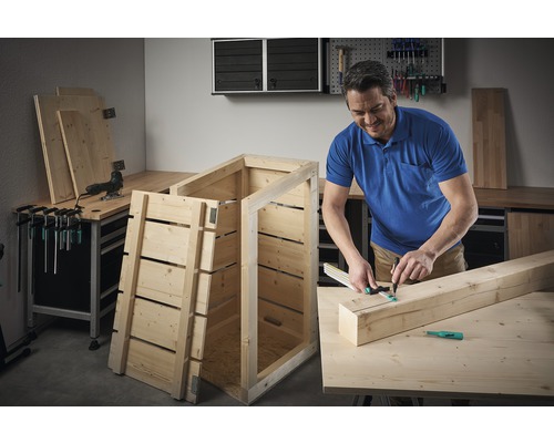Un bărbat construiește o cutie de lemn într-un atelier.